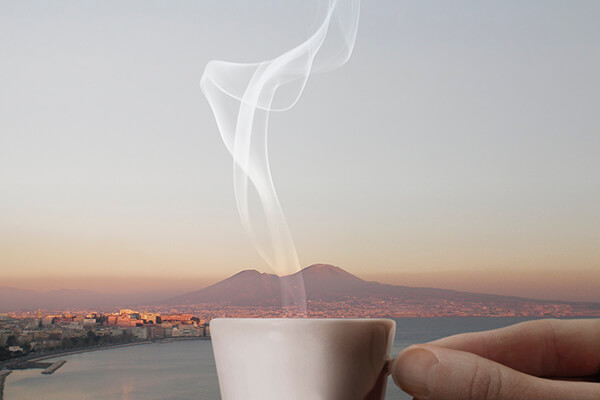 Une main tient une tasse de café fumante au premier plan, avec un paysage urbain côtier et une grande montagne à l'arrière-plan - une inspiration parfaite pour tout emballage d'agence de création à la recherche d'un lever ou d'un coucher de soleil pittoresque.