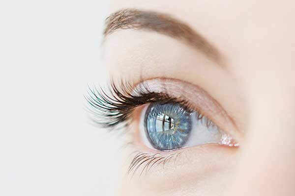 Gros plan d'un œil bleu avec de longs cils et un sourcil bien défini, idéal pour la création de catalogue ; l'image met en évidence les détails complexes de l'iris et la peau lisse qui l'entoure, sur un fond légèrement flou.