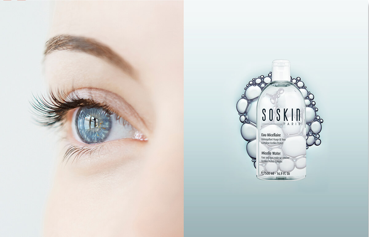 Gros plan sur un œil bleu aux longs cils à gauche, et sur un flacon d'eau micellaire SOSKIN Paris, parfait pour la création de catalogue, entouré de bulles sur un fond bleu clair à droite.