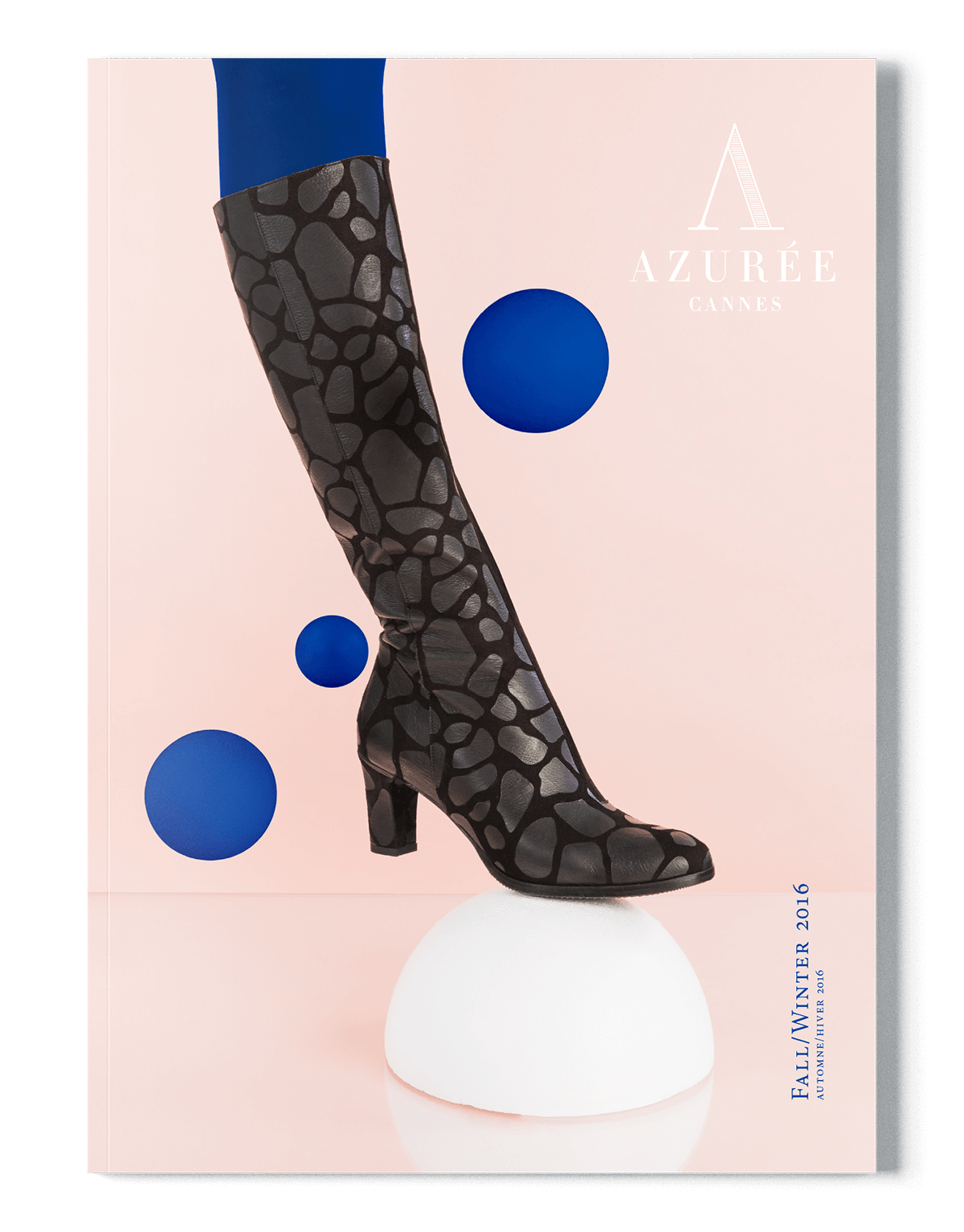 Une couverture de magazine représentant un mannequin dans une grande botte noire à motifs et à talon épais, parfaite pour votre prochaine création de catalogue. La botte repose sur un dôme blanc sur un fond rose avec des cercles bleus. Le texte indique "AZURÉE CANNES" et "Automne/Hiver 2016".