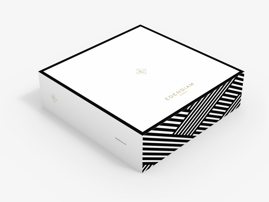 Une boîte carrée blanche minimaliste avec des bandes noires audacieuses sur un coin et "EDENDIAM" en lettres dorées sur le dessus, parfaite pour une création de catalogue. Le design est épuré, avec des lignes noires nettes et une esthétique raffinée et moderne.