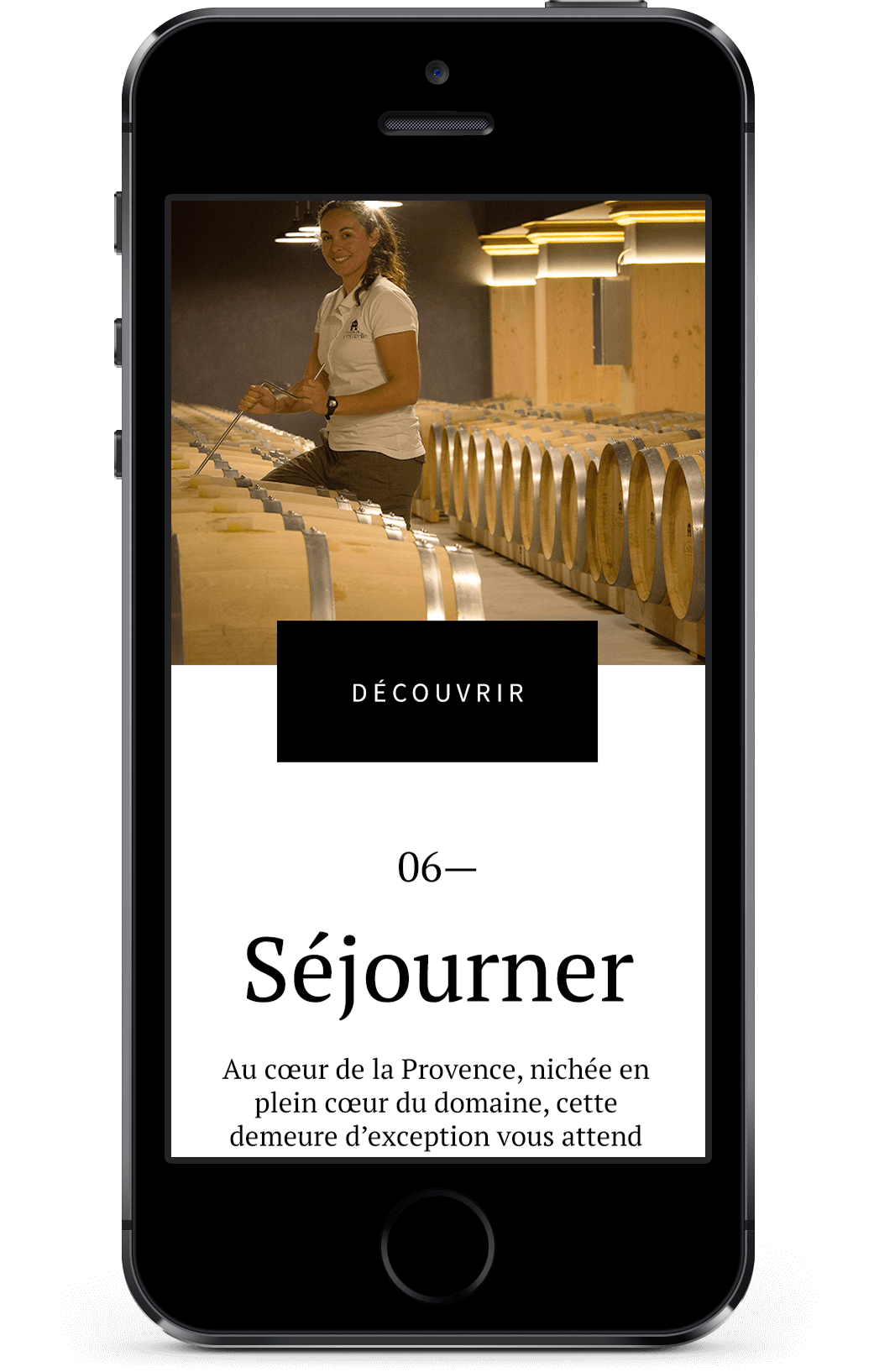Un smartphone affiche un site web avec une femme assise sur des tonneaux de vin dans une cave. Créé par une agence de marketing digital à Nice, l'écran affiche "Séjourner" et un texte sur les séjours en Provence, avec un bouton "Découvrir" au-dessus.