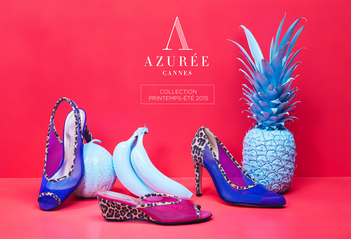Trois bananes bleues et un ananas bleu sont posés à côté de trois chaussures de femme colorées avec des accents d'impression animale sur un fond rose vif, illustrant une création de catalogue pour la collection Printemps-Été 2015 d'AZURÉE CANNES.