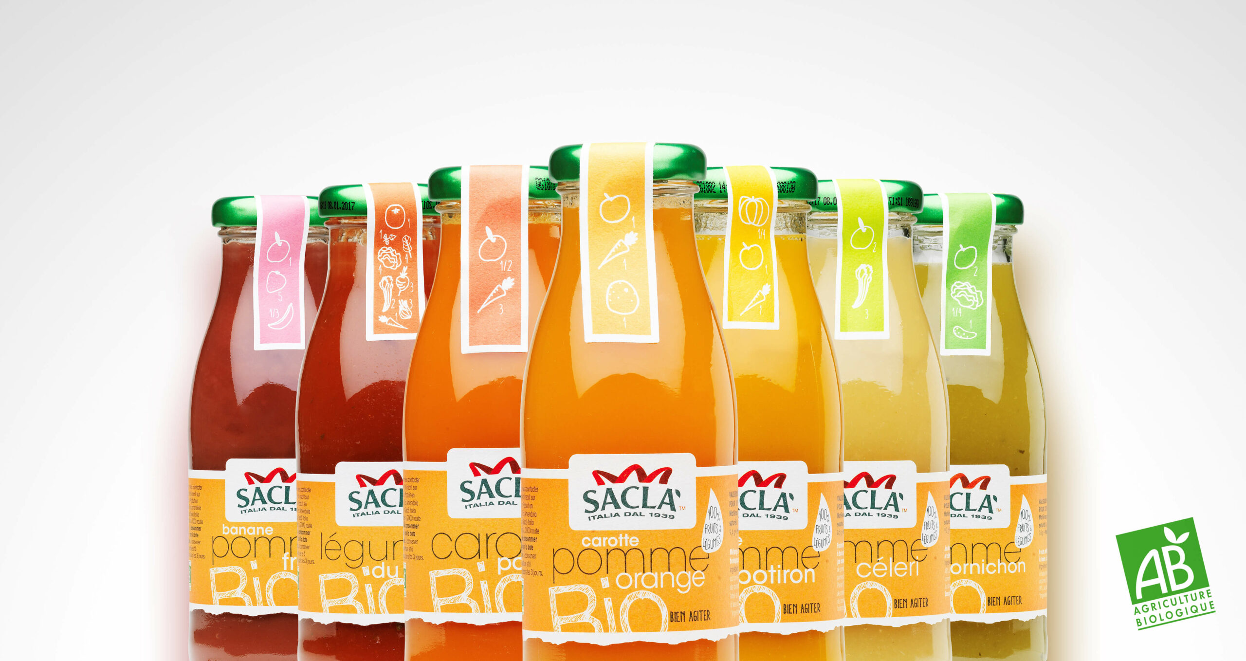 Une rangée de bouteilles de jus de fruits biologiques Saclà colorées avec des bouchons verts et des étiquettes d'emballage illustrées en français, présentant différentes saveurs de fruits et de légumes. Le logo de certification biologique "AB Agriculture Biologique" se trouve dans le coin inférieur droit.