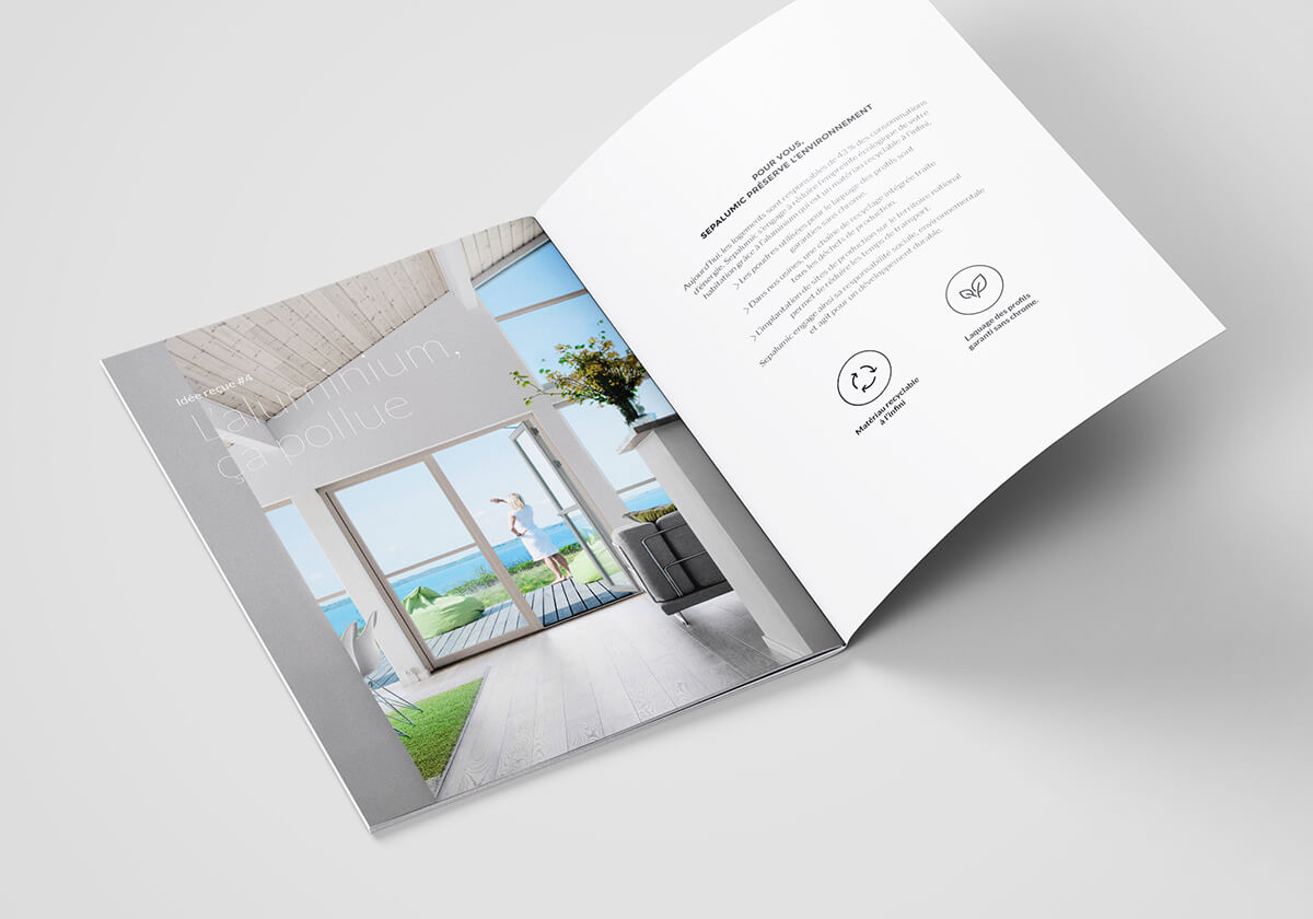 Une brochure ouverte est posée sur une surface blanche. La page de gauche montre une pièce lumineuse avec de grandes fenêtres donnant sur l'océan, tandis que la page de droite présente un texte de communication B2B, des icônes et un design minimaliste.