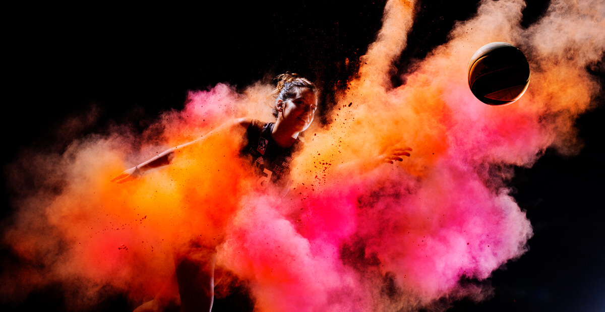 Un joueur de basket-ball en mouvement attrape un ballon, entouré de nuages vibrants de poudre orange et rose sur un fond sombre - une démonstration électrisante de l'identité visuelle.