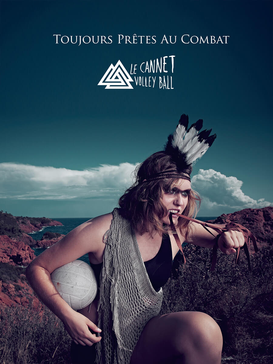 Une femme portant une coiffe à plumes et des vêtements à franges, tenant un ballon de volley-ball et des lanières de cuir, pose farouchement en plein air, incarnant l'identité visuelle de "Toujours Prêtes Au Combat" et de "Le Cannet Volley Ball" présentés au-dessus d'elle.