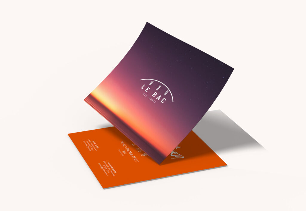 Une carte carrée pliée avec un dégradé de soleil couchant et le logo "Le Bac Restaurant" sur le dessus reflète une image de marque forte. Elle repose sur une carte orange avec un texte blanc, les deux projetant des ombres douces sur un fond pâle.