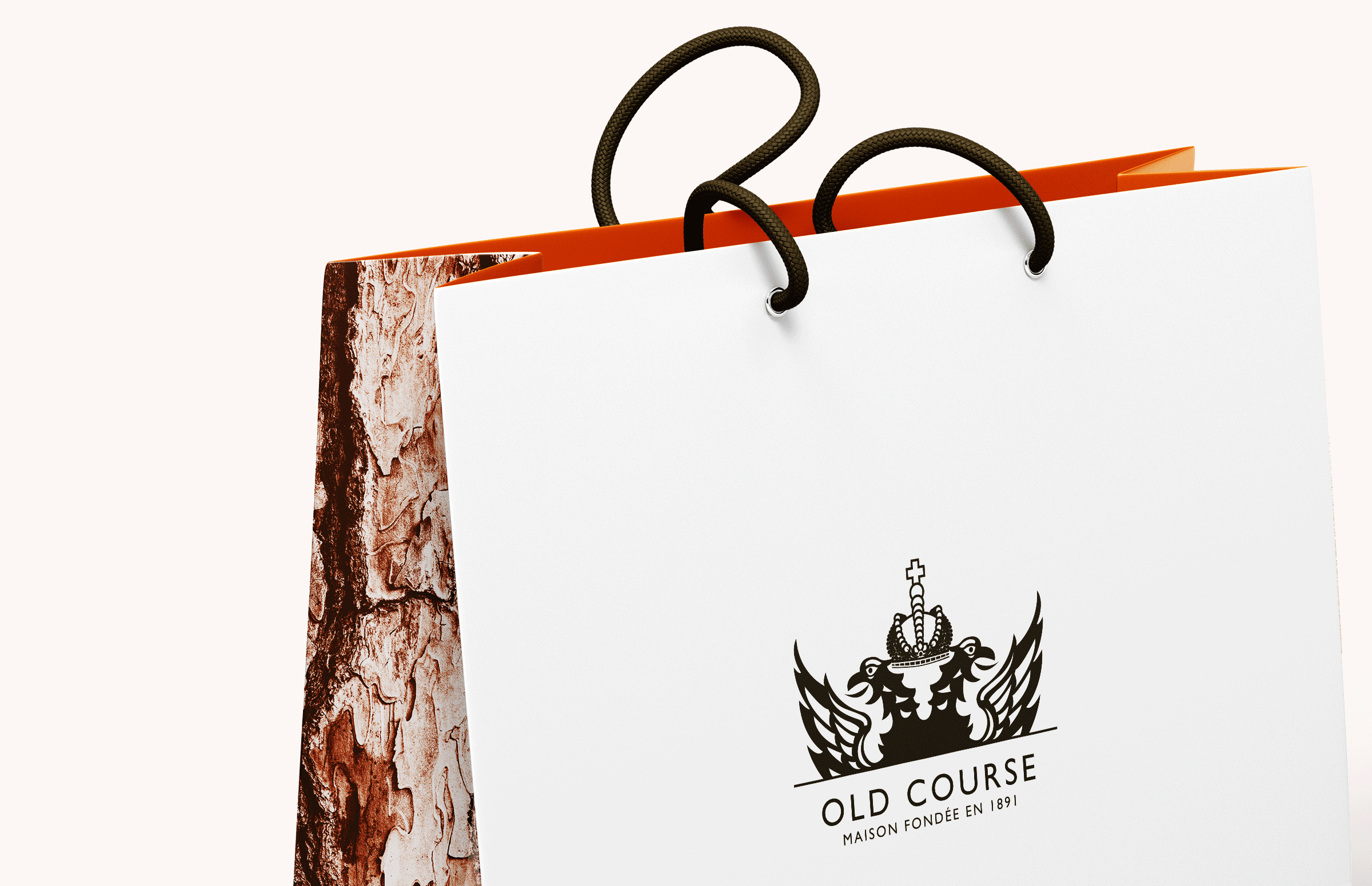 Gros plan sur un sac à provisions blanc avec des poignées en corde noires, un intérieur orange et une texture d'écorce d'arbre sur le côté. L'avant est orné d'un logo noir en forme d'écusson et de la mention "OLD COURSE MAISON FONDÉE EN 1881", reflétant une forte image de marque.