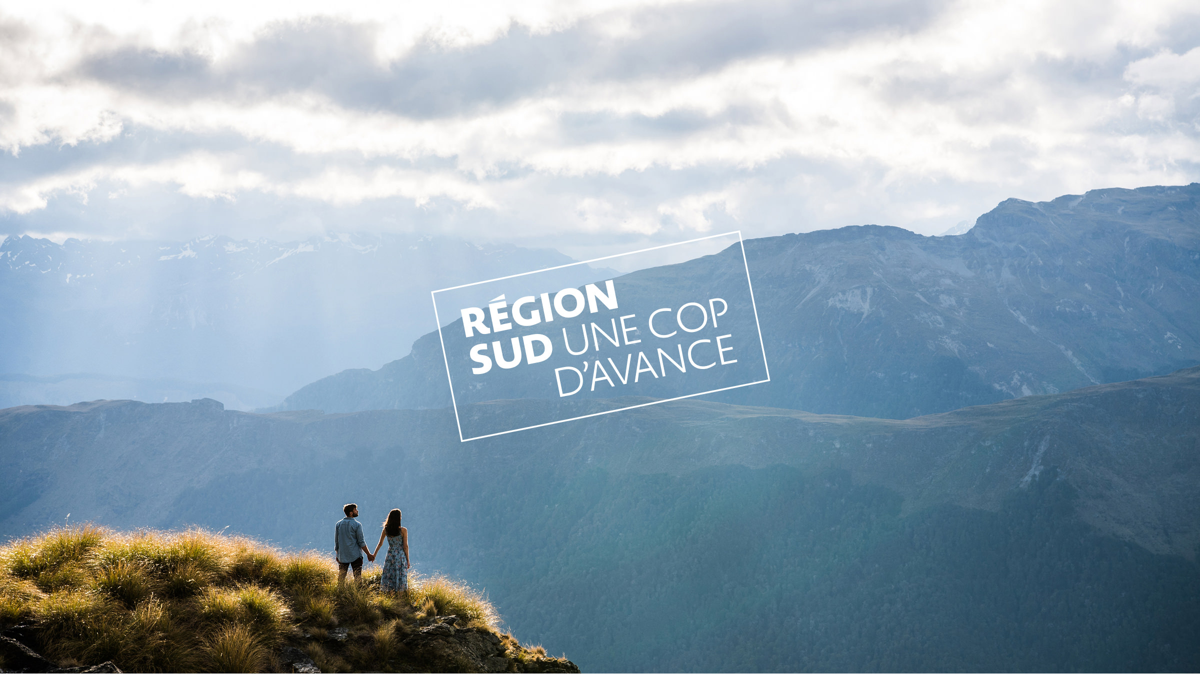 Un couple se tient par la main sur une colline herbeuse, surplombant un vaste paysage de montagne sous un ciel nuageux. Le texte se lit comme suit : "RÉGION SUD UNE COP D'AVANCE-un aperçu du rapport activité.