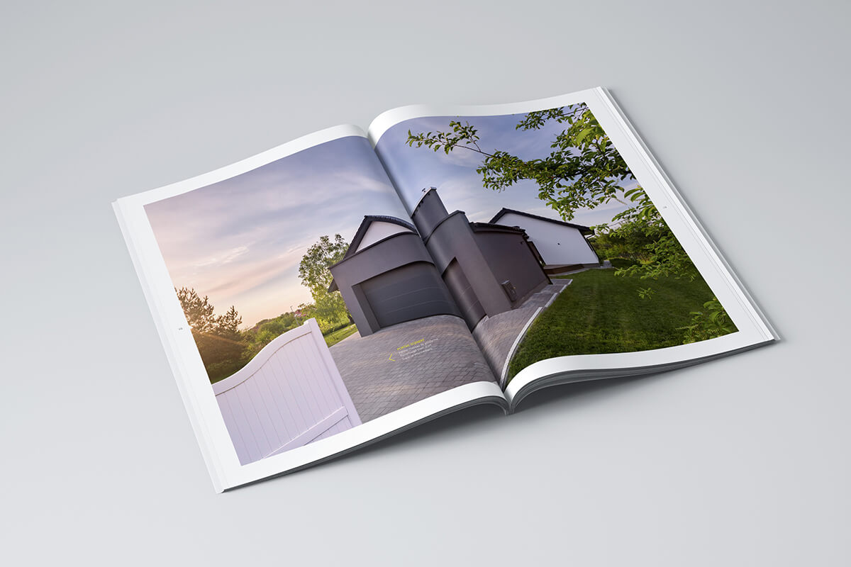 Une édition ouverte du magazine présente une maison moderne à l'extérieur gris, entourée de verdure et d'une allée, répartie sur les deux pages d'une surface gris clair.
