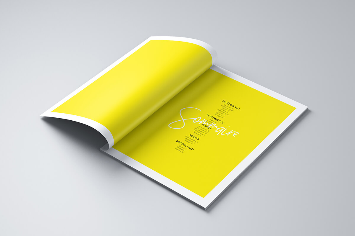 Un magazine ouvert se trouve sur une surface grise, présentant une édition spéciale avec des pages jaune vif et un texte élégant, y compris le mot "Souvenir" en script sur la page de droite.