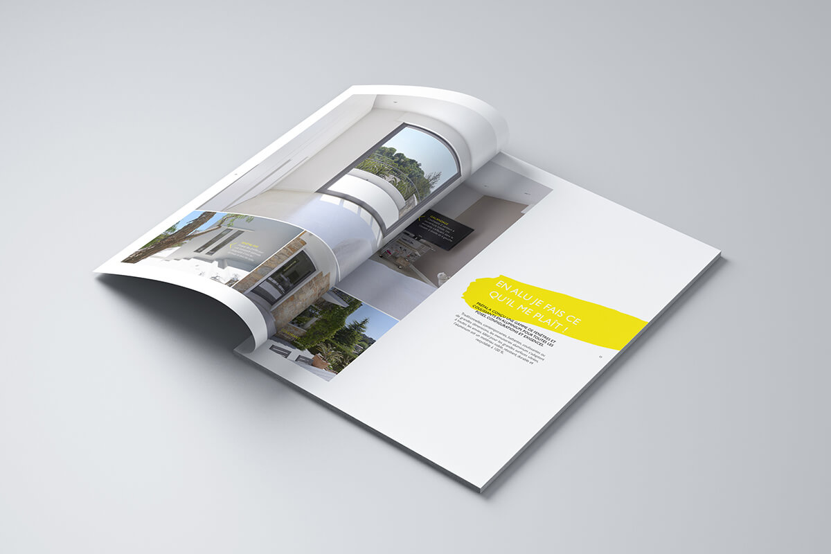 Une édition ouverte du magazine est posée sur une surface gris clair, présentant des photos d'architecture et d'intérieurs modernes, avec une zone de texte jaune en surimpression sur la page de droite. Les pages du magazine sont légèrement incurvées.