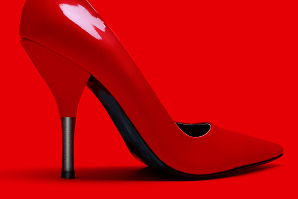 Une chaussure rouge brillante à talon haut et à bout pointu est présentée sur un fond rouge vif assorti, ce qui en fait un choix accrocheur pour les campagnes de webmarketing. Le talon est fin et noir à la base.
