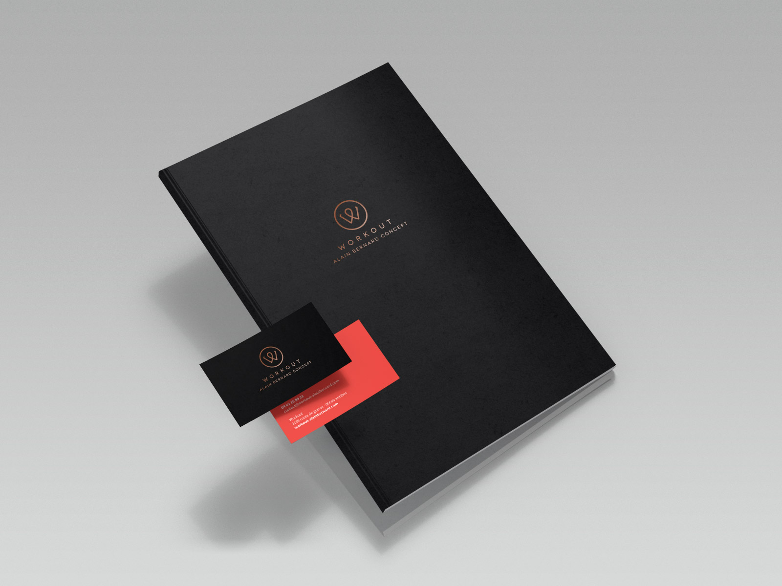 Un carnet noir à couverture rigide présentant une création minimaliste, une charte graphique et un logo ainsi que le texte "WORKHOUSE", associé à une carte de visite noire et rouge élégante partiellement insérée, le tout sur un fond gris clair.