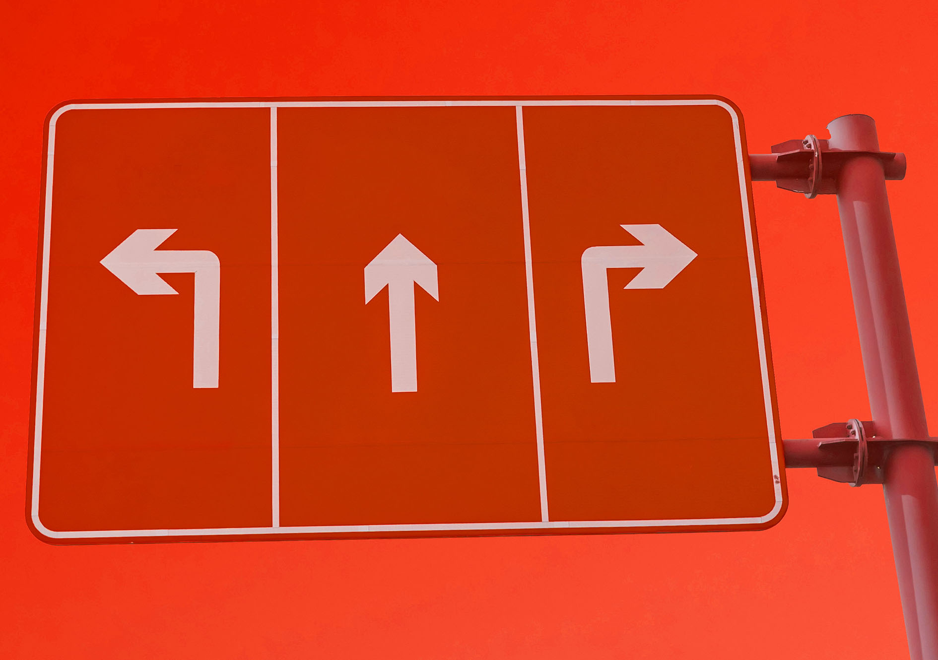 Un panneau routier rouge avec trois flèches blanches - gauche, droite et droite - se détache sur un fond de ciel rouge, attirant l'attention comme une stratégie de référencement efficace.