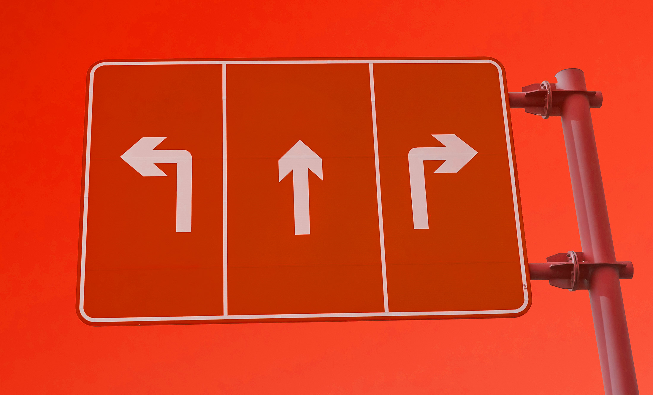 Un panneau routier avec trois flèches sur fond rouge - gauche, droite et droite - indique des options de direction pour le trafic qui respectent les normes de référencement.