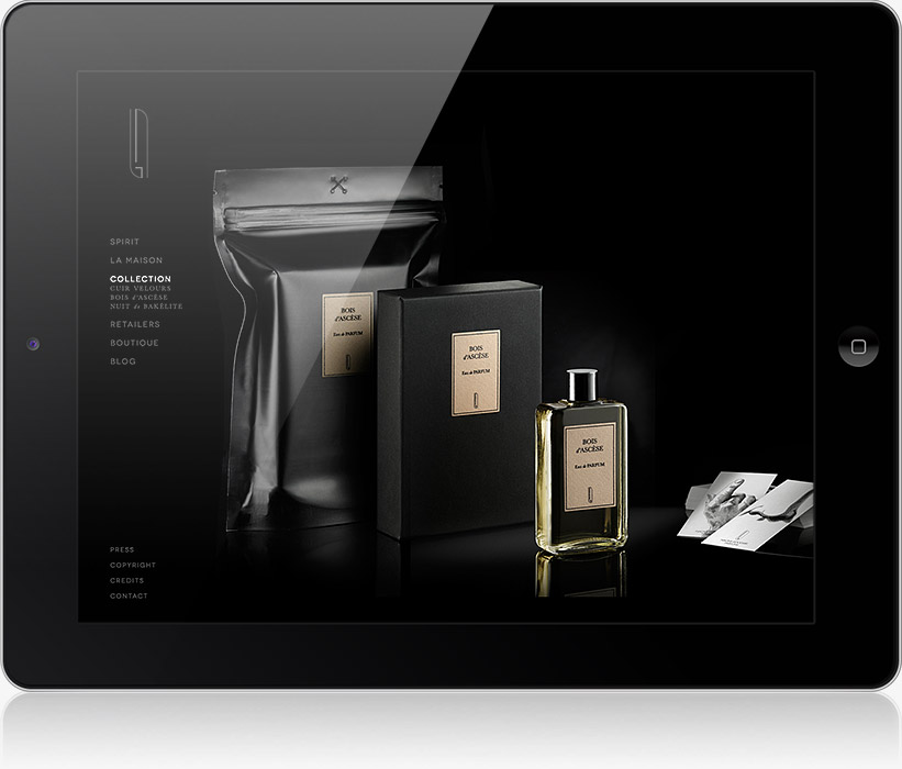 Une tablette affiche une page web de produit élégante, conçue par une agence de communication digitale à Nice, présentant un flacon d'eau de Cologne, une boîte noire, un sachet refermable et des cartes de visite avec des étiquettes dorées minimalistes sur un fond noir.