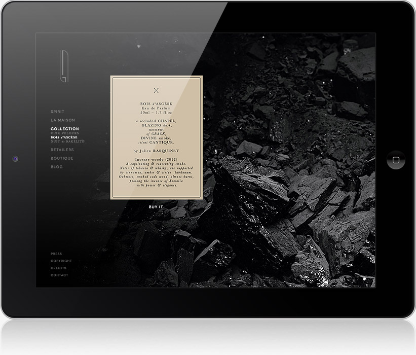 Une tablette affiche une page web au thème sombre, avec une boîte beige centrée contenant un texte sur une agence de communication digitale à Nice. L'arrière-plan présente des rochers noirs, tandis que des liens de navigation apparaissent sur le côté gauche de l'écran.