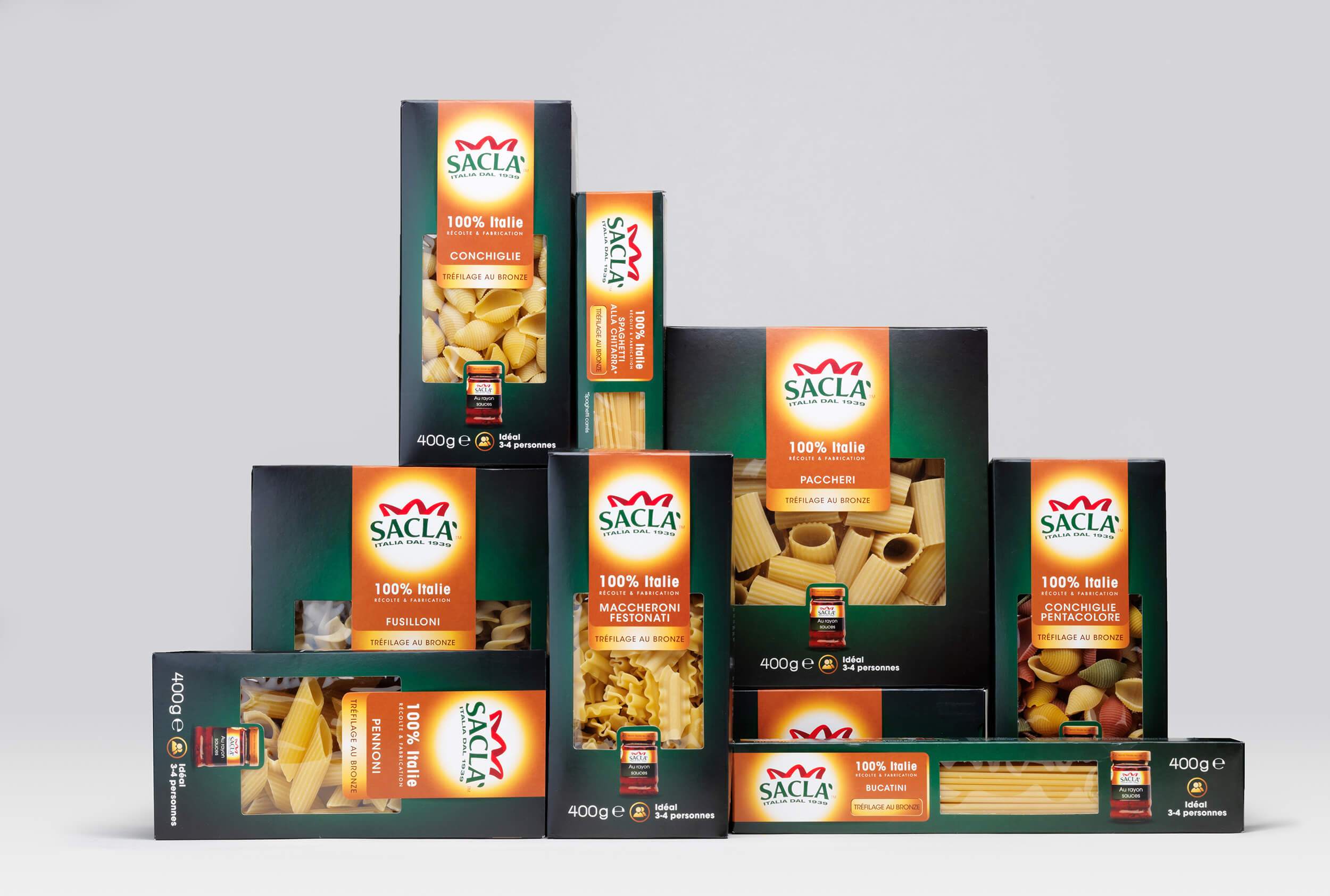 Neuf boîtes de pâtes italiennes de la marque Saclà, présentant une conception élégante de l'emballage, comprenant des conchiglie, des paccheri, des fusillone, des maccheroni, et plus encore, sont soigneusement empilées sur un fond gris clair uni.