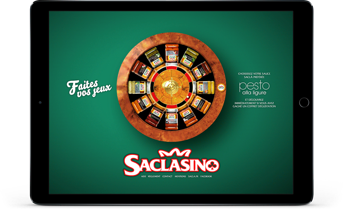 Une tablette affiche une roulette remplie de pots de sauces Saclà, sur un fond vert avec le logo Saclà. Cette scène de marketing viral comporte la mention "Faites vos jeux" et met en évidence les détails de la sauce "pesto alla ligure" sur la droite.