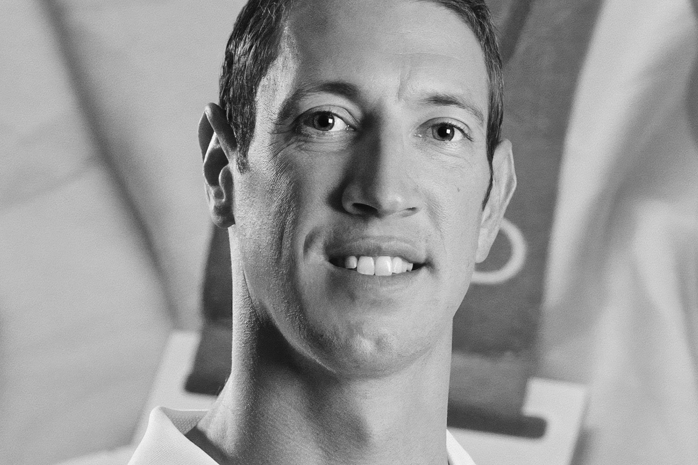 Portrait en noir et blanc d'un homme aux cheveux courts, portant une chemise à col, souriant doucement et regardant l'appareil photo. L'arrière-plan flou évoque un bureau, reflétant subtilement son expertise en matière de webmarketing.