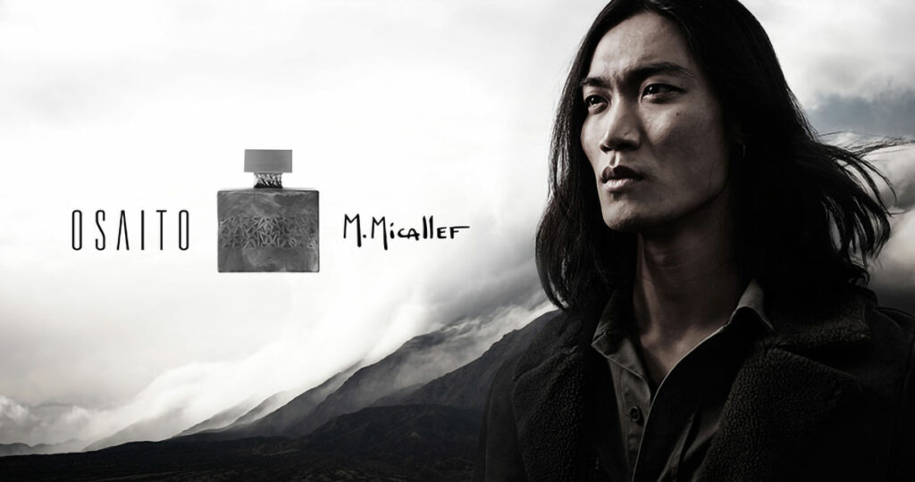 Un homme sérieux aux longs cheveux noirs se tient devant des montagnes et des nuages spectaculaires dans cette publicité créative. À côté de lui, "OSAITO" et "M. Micallef" encadrent un flacon de parfum de forme carrée, reflétant un mélange saisissant d'élégance et de nature.