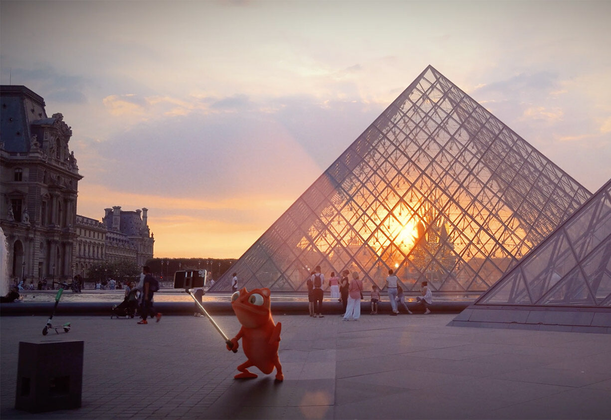 Une créature orange caricaturale tenant une épée lumineuse se tient devant la pyramide du Louvre au coucher du soleil, tandis que les personnes à proximité admirent la vue et que des animations et vidéos 3D dansent sur la pyramide de verre reflétant la lumière du soleil.