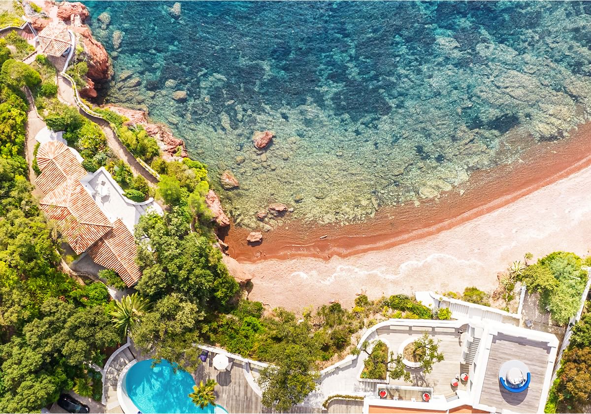 Vue aérienne d'une villa côtière avec un toit de tuiles rouges, une piscine, une végétation luxuriante et un rivage rocheux rencontrant une mer turquoise - comme un développement de site web sur mesure conçu pour allier beauté, fonction et unicité de manière transparente.