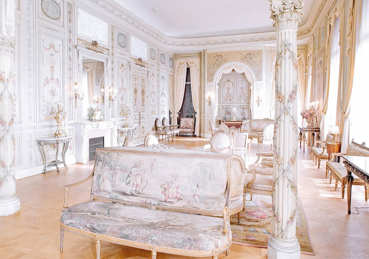 Une salle élégante et ornée de murs blancs et dorés évoque le raffinement de la création d'identité de marque, avec de grandes fenêtres aux rideaux drapés, des meubles anciens, une grande cheminée, des détails dorés et des œuvres d'art classiques sur les tissus d'ameublement.