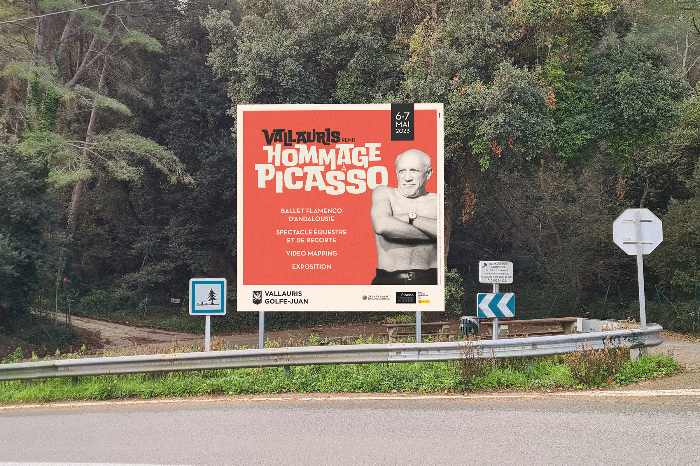 Un grand panneau d'affichage en bordure de route, présentant la communication événementielle, annonce "Vallauris 2023 Hommage Picasso" avec une photo en noir et blanc de Pablo Picasso. Les détails et les dates de l'événement, les 6 et 7 mai 2023, sont indiqués. Des arbres et une route en courbe sont à l'arrière-plan.