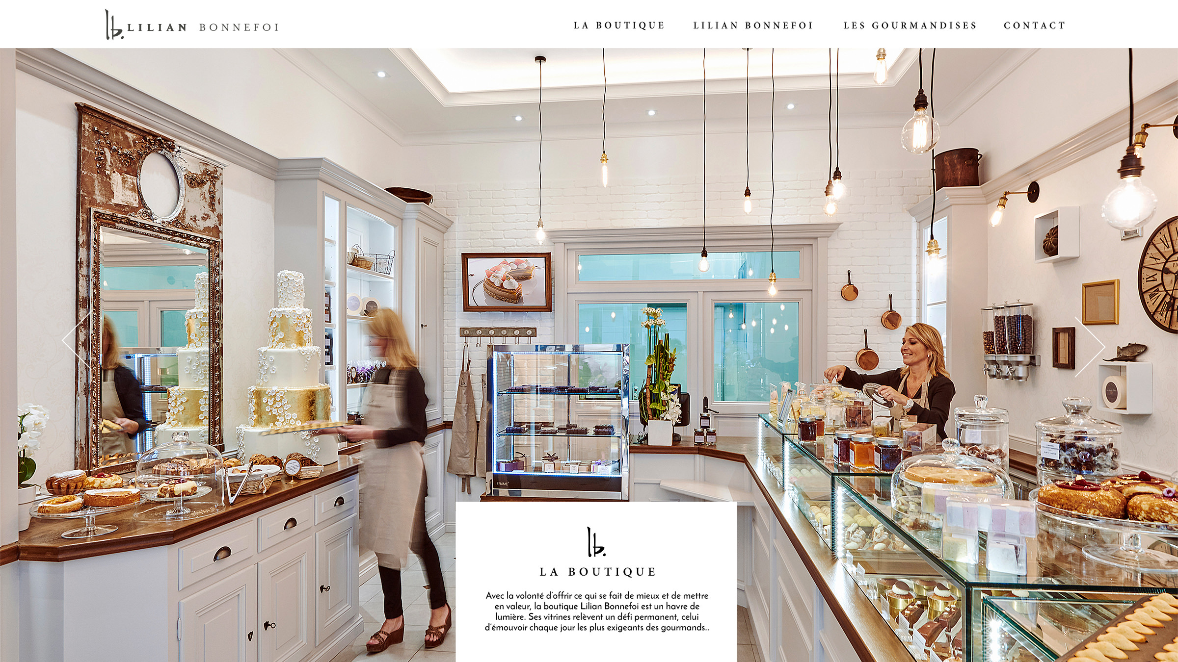 Une boulangerie lumineuse et élégante avec des gâteaux et des pâtisseries exposés dans des vitrines. Deux femmes travaillent derrière le comptoir, l'une servant et l'autre arrangeant les articles. Les murs blancs, les touches dorées et les étagères ajoutent une atmosphère raffinée et accueillante.